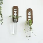 Dekorativ väghängare i metall med design inspirerad av månens faser, innehållande gröna växter för en naturlig och modern touch.