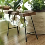 Hängande balkonglåda med gröna växter i en glasvas, stöd i trä och metall, naturlig och modern inredning.