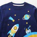 Barnkläder med rymdmotiv, inklusive raket, stjärnor, planet och teleskop, perfekt för astronomi- och rymdutforskningsentusiaster.