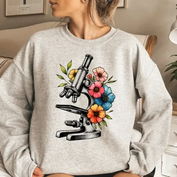 Mikroskop illustrerat med färgglada blommor på en grå sweatshirt, som kombinerar vetenskap och natur i en modern och trendig stil.