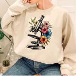 Sweatshirt med mönster av mikroskop omgiven av färgglada blommor, perfekt för vetenskaps- och originalinredningsälskare.