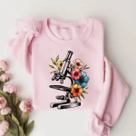 Kolla in denna illustration av mikroskop omgiven av färgglada blommor, perfekt för en original och vetenskaplig t-shirt.