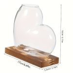 Hjärtfomad transparent glasvas med träbas, perfekt för vetenskaplig eller romantisk dekoration. Mått: 13 cm hög, 17 cm lång, 5,5 cm bred.