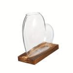 Transparent glasvas i hjärtform, placerad på en bas av naturligt trä, idealisk för vetenskaplig eller konstnärlig dekoration.